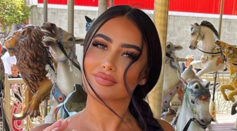 Jessica Foster embodies effortless resort-glam elegance, pairing a sun-kissed beauty aesthetic with a flawlessly defined, soft nude lip. Her face-framing waves and minimalist warm-weather styling create a sophisticated, photogenic contrast against the playful carousel backdrop.